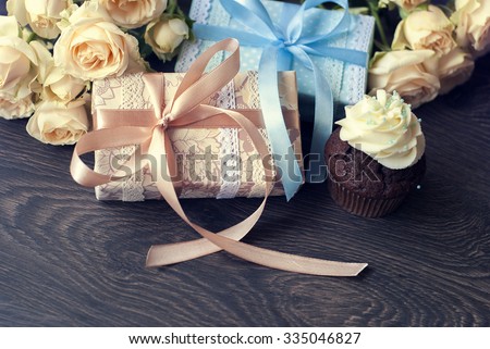 Ashy roses, packed gifts and chocolate cupcake with sprinkles and blue cream on dark table.
