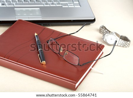 The laptop an organizer a pen and clock on desk