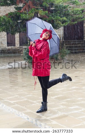 Young  beautiful caucasian woman with an umbrella dressed in Red and  dancing in the rain.