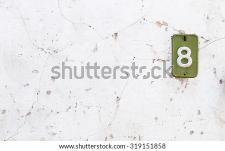 White abstract wall background with house nember of eight in a green metal frame