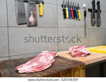 Meat on butchers cutting board and sharp knives hanging on the wall