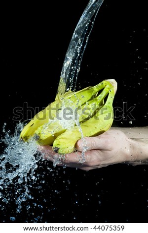 Hand and banana with splashing water on black background