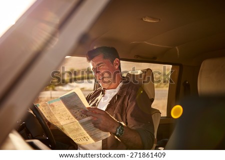Mature man sitting in the driver\'s seat of his car, looking at a map in confusion while he is trying to figure out directions for his journey. The shot has been taken from outside of the vehicle