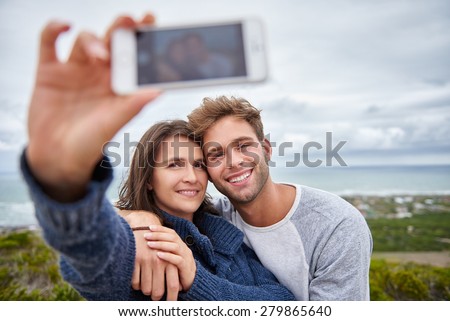 Loving boyfriend and girlfriend posing for a selfie on their phone while on a nature walk along a beautiful coastline on a calm overcast day