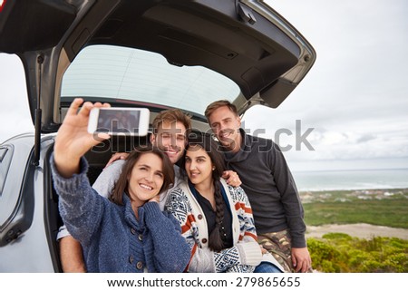 Group of friends taking a roadtrip along the coast posing for selfie at the back of their car