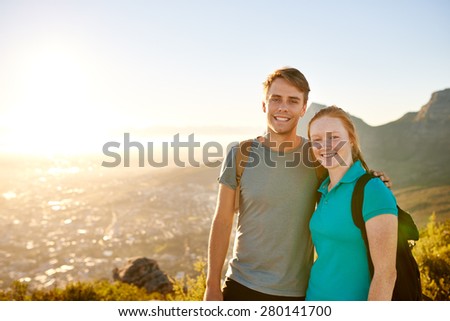Smiling young couple posing together with a picturesque view behind them while on a hike on a nature trail