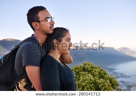 Side view of a loving young Indian couple standing closely together while on a nature hike and looking into the distance