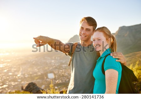 Handsome young guy standing with his girlfriend pointing to something in the distance while on a nature hike together