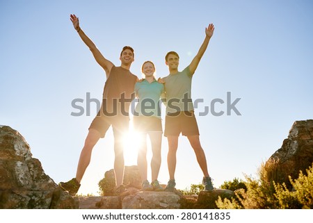 Low angle shot of three athletic friends standing on a rocky mountain and posing triumphantly