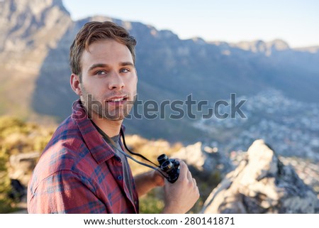 Handsome young guy holding binoculars and looking back briefly while standing in a natural setting