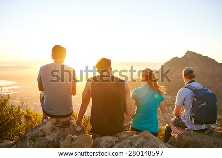 Rearview of a row of friends sitting on a nature trail watching the sunrise together