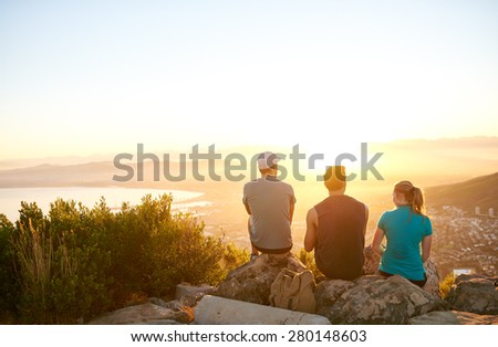 Three friends watching the sunrise over the city together from a mountain nature trail