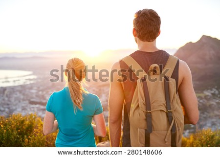 Rearview of a guy and girl standing next to each other watching the sunrise while on a nature hike together