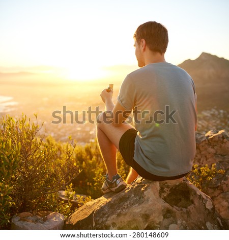 Rearview shot of a young guy on a nature trail pausing to eat a protein bar while watching the sunrise