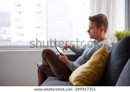 Profile shot of a handsome guy on his couch at home using his digital tablet