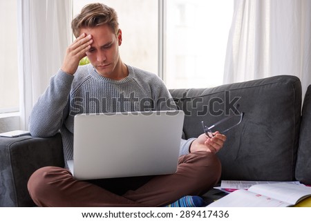 Guy on his couch at home looking at his laptop with a worried expression