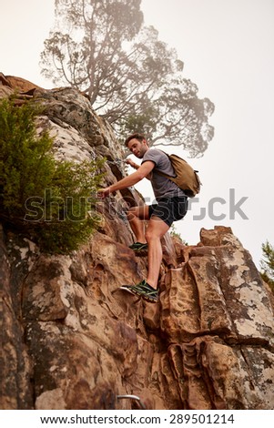 Low angle shot of a male hiker carefully climbing rocks on a mountain nature trail where chains have been provided for assistance