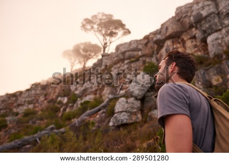 Low angle shot of a young man walking on a nature trail with a view of the misty mountain top beyond him