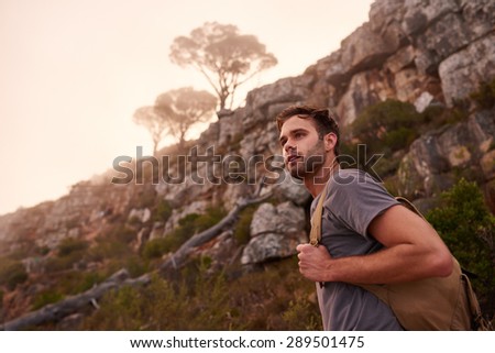 Low angle shot of a young male hiker on a nature trail with the misty mountain top and trees behind him