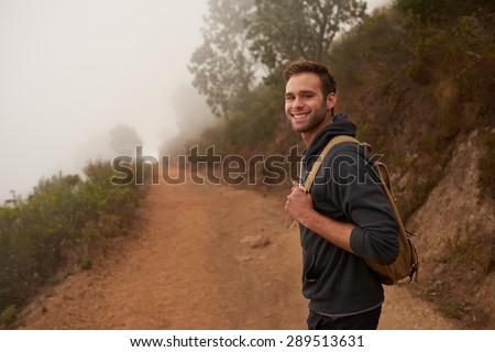Young male hiker looking back at the camera and smiling while on a nature hike on a misty morning