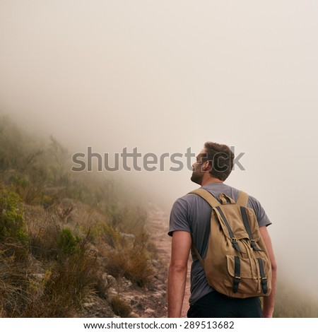 Rear view of a young man on a mountain path looking up on a misty morning