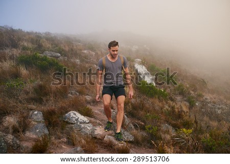 Full length shot of a young male hiker stepping carefully over stones while on a mountain nature trail on a misty morning