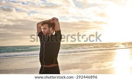 Handsome young man on the beach in the morning stretching his muscles before a run
