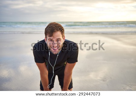 Fit young man smiling and taking a quick rest while enjoying a run on the beach in the early morning