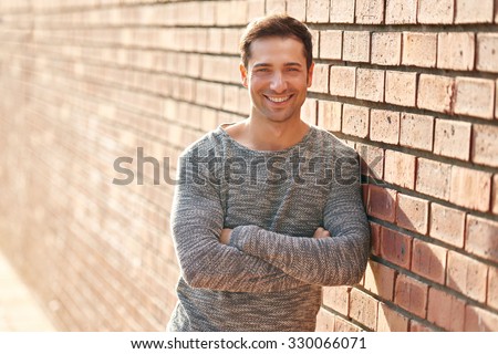 Handsome man with a friendly smile leaning casually against a brick wall with a rough texture outdoors