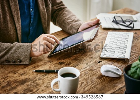Cropped shot of the hands of a trendy young businessman using a digital tablet at his neat office desk