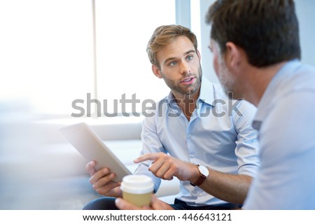 Handsome young business entrepreneur holding a digital tablet while talking about ideas with his mature corporate manager