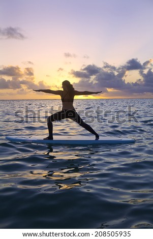 woman doing yoga on a stand-up paddle board in the ocean at sunrise