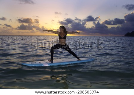 woman doing yoga on a stand-up paddle board in the ocean at sunrise