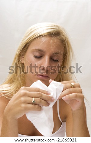 a young woman with a head cold using a tissue to blow her nose