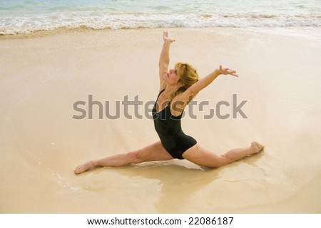 A fifty year old woman doing yoga and stretches on the beach by the ocean in Hawaii at daybreak.