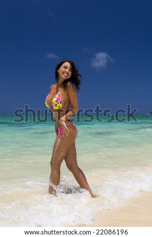 A beautiful young dark haired woman in a yellow bikini smiling playing at the seashore on a Hawaii beach.