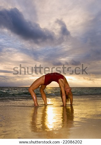 A fifty year old woman doing yoga and stretches on the beach by the ocean in Hawaii at daybreak.