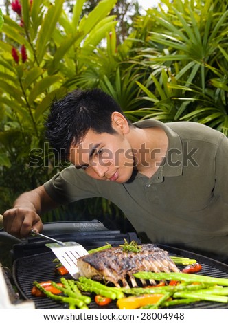 A young Asian American man grilling rack of lamb on a barbecue in his yard