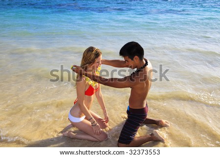 Hawaiian beachboy gives a flower lei to a blond girl in a bikini at the beach