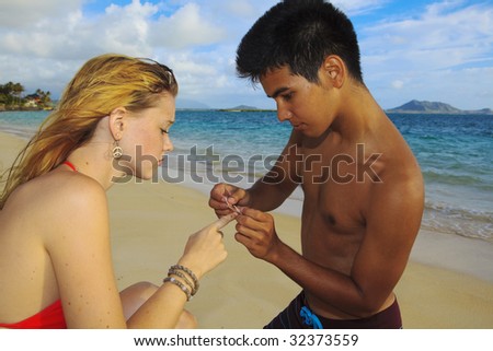 Hawaiian man puts a bandage on the finger of a blond girl at the beach