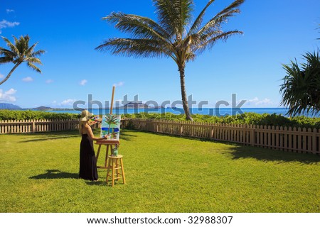 A female artist in her fifties creating a painting outside on canvas of a palm tree and the ocean in Lanikai, Hawaii