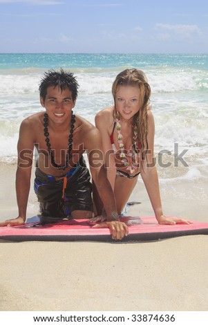 A young Hawaiian man and a blond girl visiting the islands kneel on a boogie board by the ocean at the beach in Kailua talking to each other