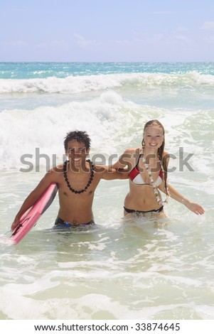A young couple comes out of the ocean with a boogie board at Kailua Beach, Hawaii