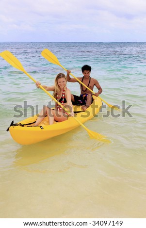A Polynesian man and a blond caucasian girl, wearing leis, paddle their ocean kayak towards shore