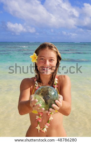 teenage girl by the ocean in hawaii with a green glass fishnet ball that broke loose from its net many years ago, and drifted across the Pacific.