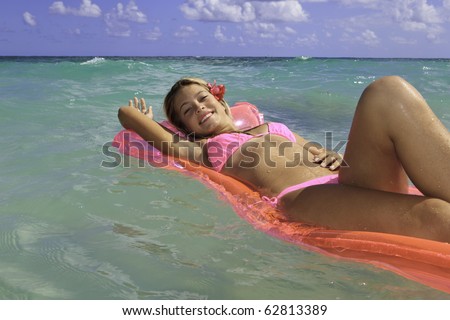 teenage girl in pink bikini floating on a pink raft in the ocean