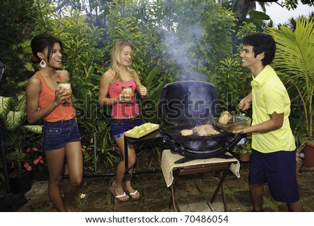 three friends at a barbecue party in hawaii cooking chicken on the grill