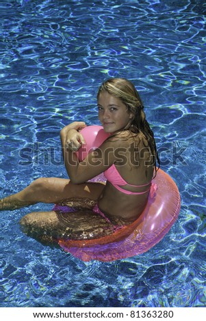 teenage girl in pink bikini playing in a pool on a pink tube, holding a pink ball