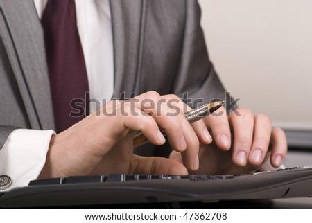 Close-up of male hands with pen typing on black computer keyboard