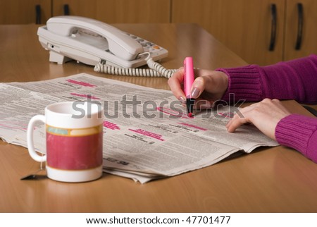 Person looking for work in the newspaper. Person is holding a bright pink highlighter pen and circling interesting jobs whilst drinking a cup of coffee.